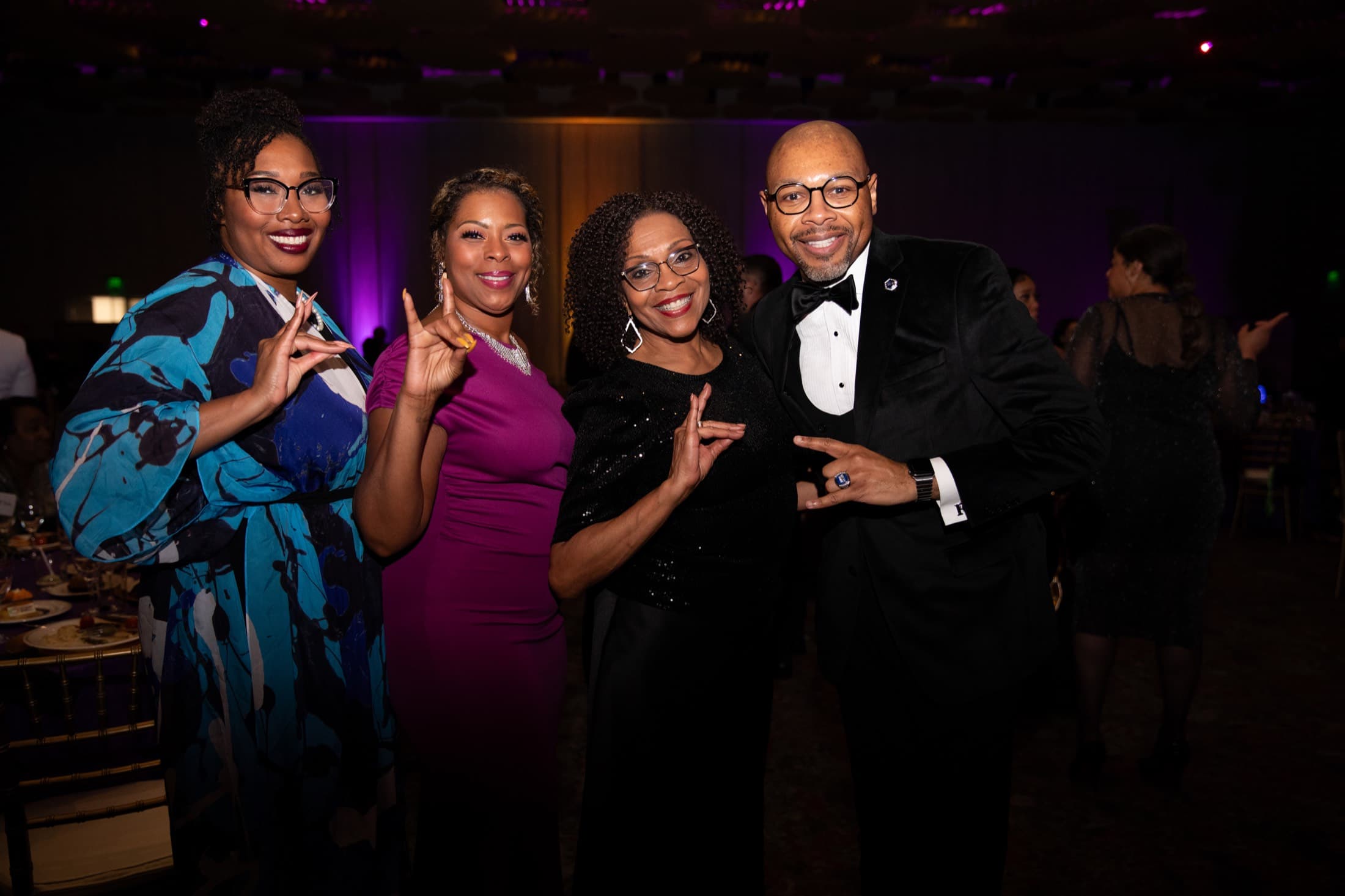 Four formally dressed guests posing at a gala with purple uplighting